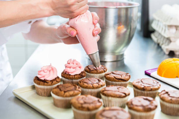 Women in pastry bakery as confectioner glazing muffins with icing bag Women in pastry bakery as confectioner glazing muffins with icing bag, close-up pastry dough stock pictures, royalty-free photos & images
