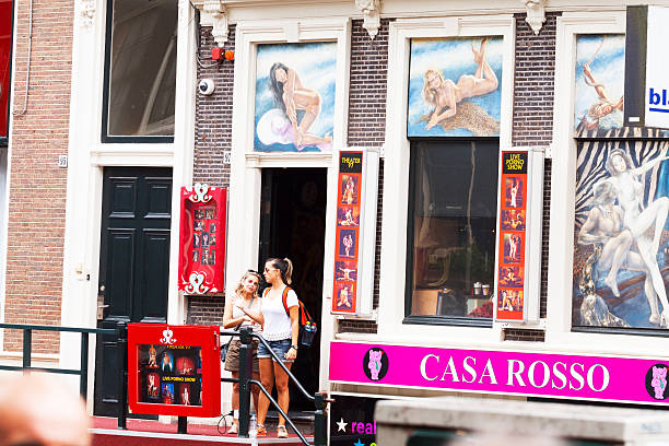 Women leaving live porno show Amsterdam, The Netherlands - June 9, 2014: Two adult women and toruists are leaving live porno show and Theater 97 in Amsterdam in Achterburgswal. Around windows are many porn images.In front of women are photos of sex show. Summer shot, live sex shows stock pictures, royalty-free photos & images