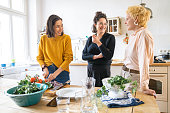 Cheerful women talking while preparing food. Happy friends are spending leisure time together. They are in casuals at home.