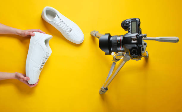 Women reviews new white sneakers with camera on tripod on yellow background. Top view. Minimalism stock photo
