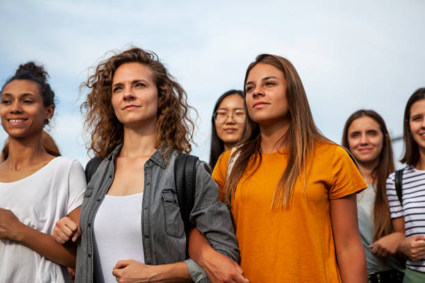 Women standing together Group of young female protestors with arms in arms and clenching fist while standing together outdoors women's rights stock pictures, royalty-free photos & images