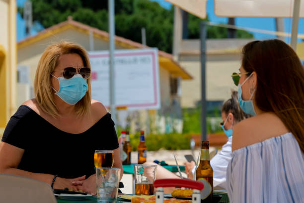 women using surgical masks and sunglasses sitting at an outdoor bar terrace - wheelchair street happy imagens e fotografias de stock