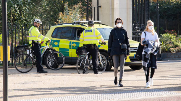 Women wearing masks, police officers on bikes and ambulance on Pall Mall during coronavirus crisis London, UK - April 4th 2020:  Girls crossing the street wearing masks with police officers on cycles talking with ambulance staff near James' Park in central London during lockdown central london stock pictures, royalty-free photos & images