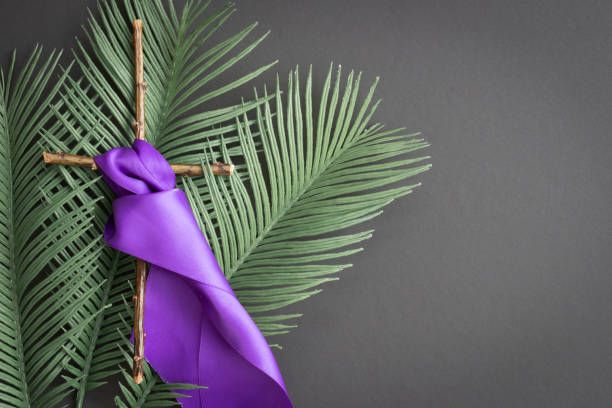 wood cross with purple ribbon on black Wood christian cross on lent palm leaves with purple ribbon or sash on black background with copy space lent stock pictures, royalty-free photos & images