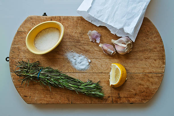Wood cutting board with fresh rosemary, salt, lemon and garlic stock photo