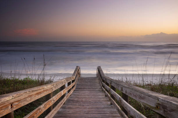 A wood pedestrian bridge, build over a sand dune that is used to give beach access in Daytona Beach, Florida, glows during a morning sunrise. stock photo