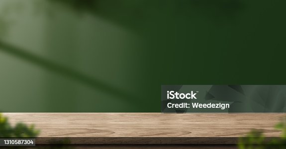 istock wood table green wall background with sunlight window create leaf shadow on wall with blur indoor green plant foreground.panoramic banner mockup for display of product.eco friendly interior concept 1310587304