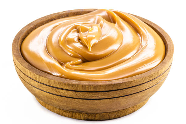 wooden bowl with homemade dulce de leche, condensed cream or pasty caramel, isolated white background. stock photo