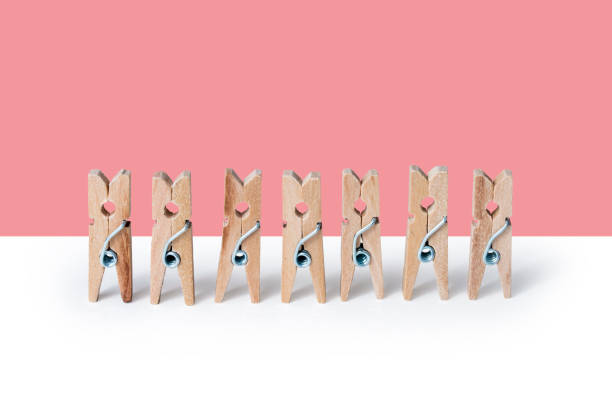 Wooden clothespins standing in a row on a pink and white background stock photo
