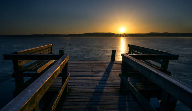 Photo of Wooden jetty with benches on a frozen lake in the light of the golden rising sun, beautiful landscape scenery, concept for a new beginning every day, copy space