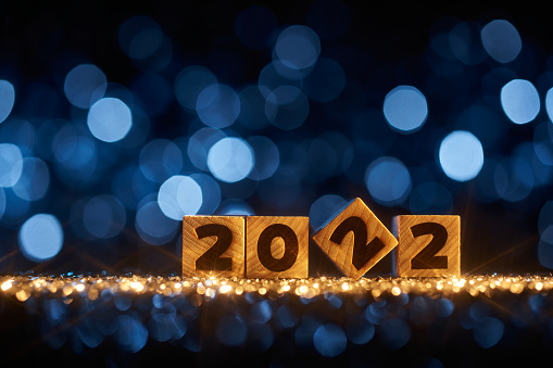 Abstract Christmas / New Year 2022 background. Wooden numbers on shimmering glitter, shiny stars, and wonderful defocused lights in a yellow blue contrast.
