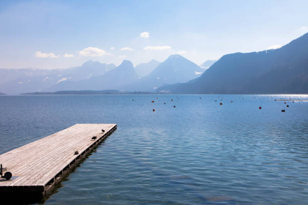 Wooden pier with calm water and Mountain range in the background. Tourism and vacations concept. Upper Austria Panoramic view of an austrian lake with wooden pier and mountain range in the background. Salzkammergut Upper Austria fuschl lake stock pictures, royalty-free photos & images