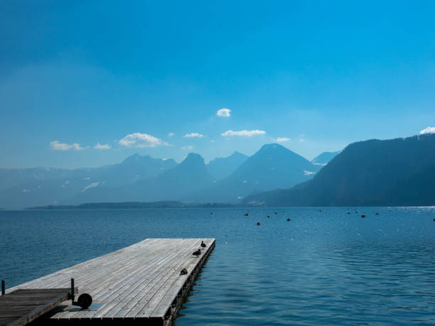 Wooden pier with calm water and Mountain range in the background. Tourism and vacations concept. Upper Austria Panoramic view of an austrian lake with wooden pier and mountain range in the background. Salzkammergut Upper Austria fuschl lake stock pictures, royalty-free photos & images