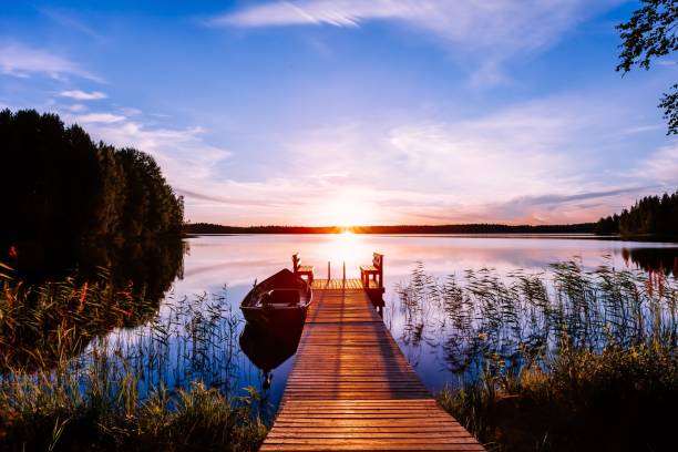 muelle de madera con barco de pesca al atardecer en un lago en finlandia - lago fotografías e imágenes de stock