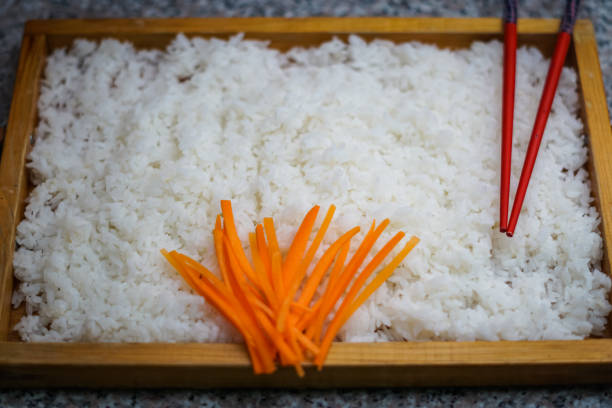 A wooden plate of rice with carrots and chopsticks stock photo