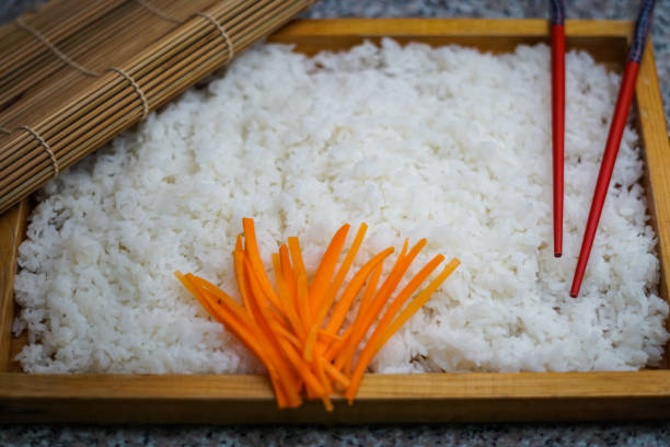 A wooden plate of rice with carrots and chopsticks stock photo