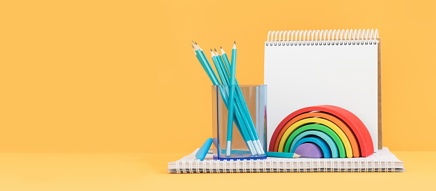 Wooden rainbow with pencils and a sketchbook. Banner on orange yellow. Art and craft. Summer or spring mood. Back to school. Copy space.