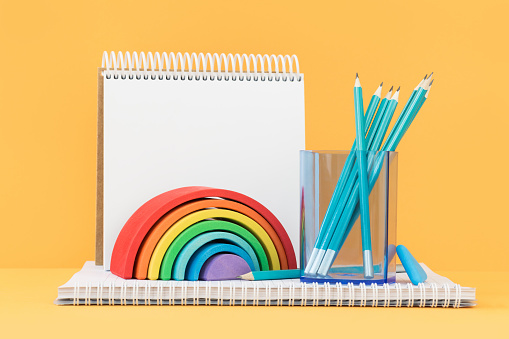 Wooden rainbow with pencils and a sketchbook. Banner on orange yellow. Art and craft. Summer or spring mood. Copy space.