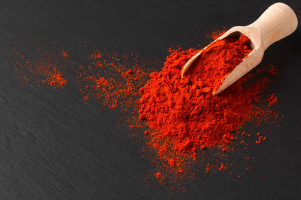 Wooden scoop with ground paprika on black textured background, close up stock photo