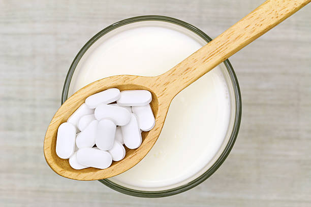Wooden spoon of Calcium carbonate tablets above glass of milk stock photo