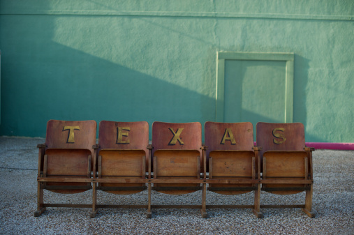 Antique wooden stadium seating with the word TEXAS painted with gold letters on the seat backs of the chairs.