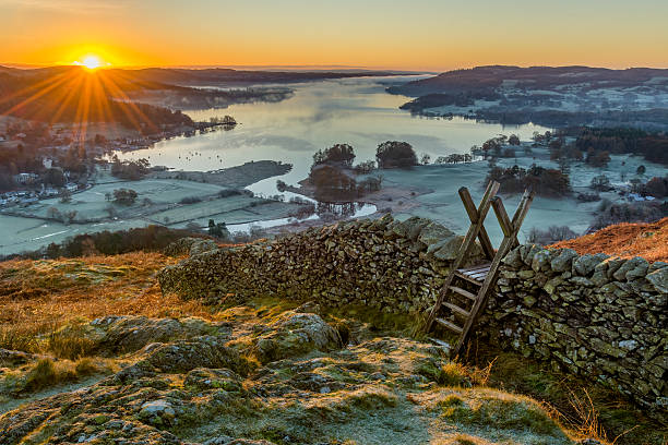 Wooden stile over stone wall with beautiful sunrise. Wooden stile and stone wall with Lake Windermere in background with sun rising above horizon. english lake district stock pictures, royalty-free photos & images