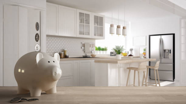 Wooden table top or shelf with white piggy bank with coins, scandinavian white and wooden kitchen, expensive home interior design, renovation restructuring concept architecture stock photo