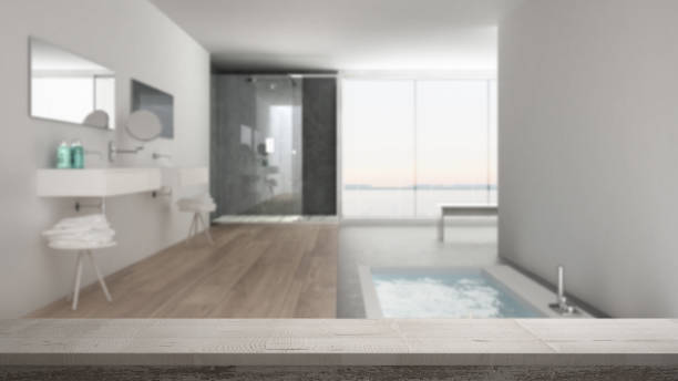 Wooden vintage table top or shelf closeup, zen mood, over blurred minimalist white bathroom with bath tub and panoramic window, white architecture interior design stock photo