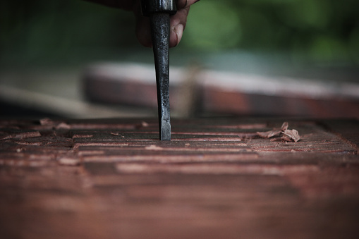 A chisel carves detail into natural wood in an outdoor setting