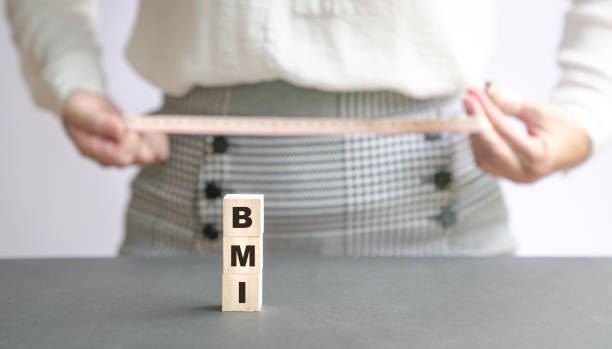 BMI word on wood cubes with woman measuring waist hip with a tape at the background. stock photo