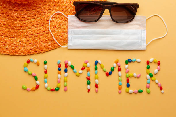 Word summer written with colorful candies on orange background with protective face mask and summer hat for seaside stock photo