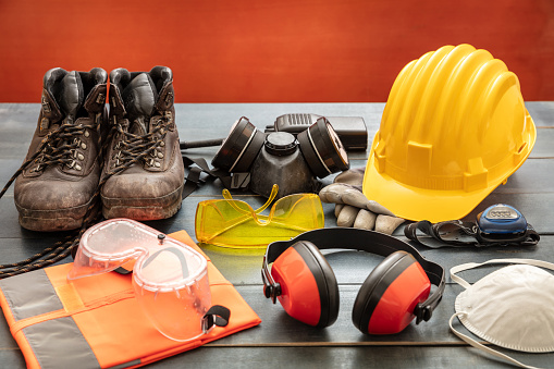 Work safety protection equipment. Industrial protective gear on wooden table, red color background. Construction site health and safety concept