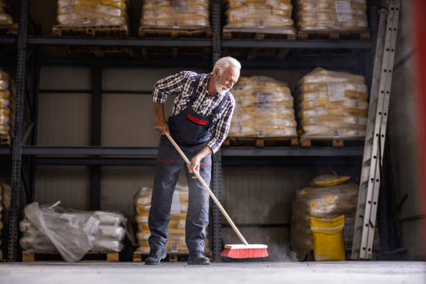 Workday in the factory. A senior factory worker is brooming factory hall. stock photo
