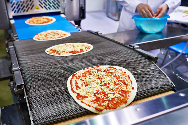 Worker cook and pizza conveyor Worker baker cook adds cheese to the pizza on the conveyor conveyor belt photos stock pictures, royalty-free photos & images