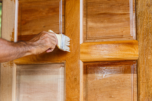 Worker Hand Painting Wooden Door With Paintbrush Linseed Oil Varnish Paint On Wood Stock Photo