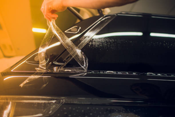 Worker hands installs car paint protection film wrap. stock photo