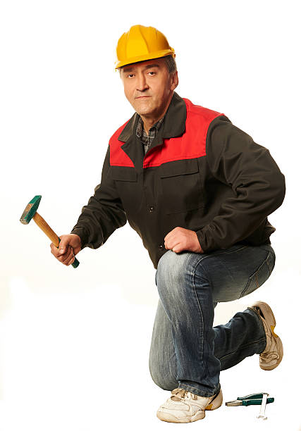 Worker in a yellow hard hat crouched with a hammer stock photo