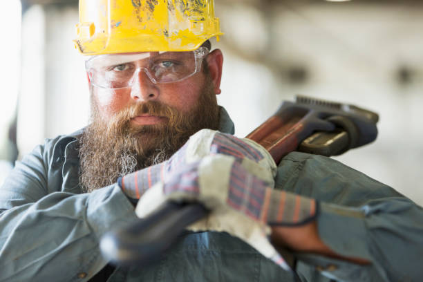 Worker in factory carrying work tool A bearded man working in a metal fabrication plant, carrying a large metal tool on his shoulder. toughness stock pictures, royalty-free photos & images
