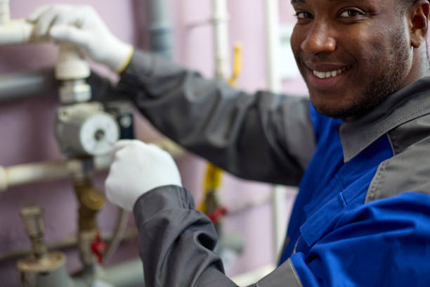 Worker in overalls adjusts the sensors in the boiler room with a screwdriver. Happy professional black worker in overalls adjusts the sensors in the boiler room using a screwdriver. Close-up of an African American man engaged in maintenance of equipment in a boiler room african american plumber stock pictures, royalty-free photos & images
