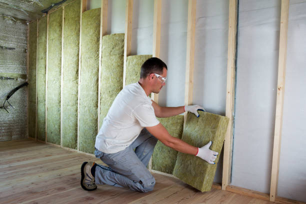 Worker in protective goggles and respirator insulating rock wool insulation in wooden frame for future house walls for cold barrier. Comfortable warm home, economy, construction and renovation concept stock photo