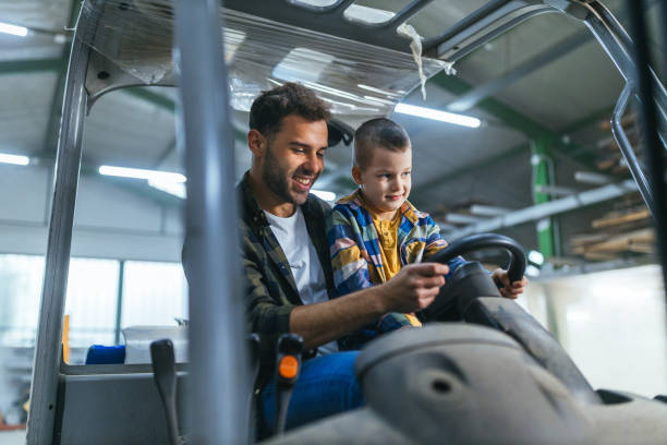 Worker in warehouse teaching his son how to drive forklift Man who works in warehouse showing to his son how to drive forklift fathers day stock pictures, royalty-free photos & images