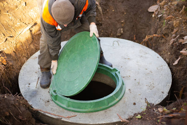 A worker installs a sewer manhole on a septic tank made of concrete rings. Construction of sewerage networks for country houses stock photo
