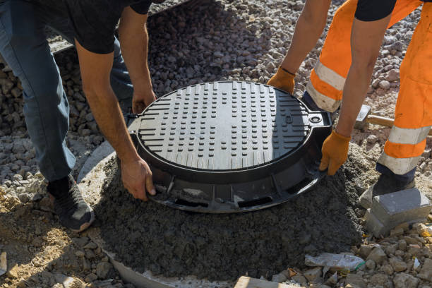 A worker installs a sewer manhole on a septic tank made of concrete rings stock photo