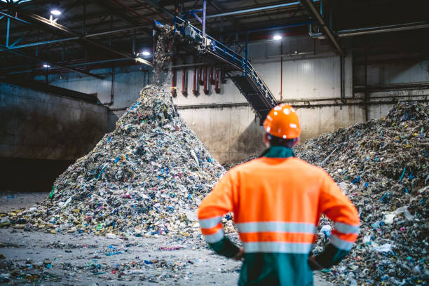 worker observing processing of waste bij recycling facility - afval stockfoto's en -beelden