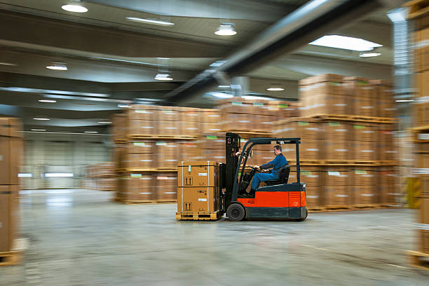 Worker on a lift truck arranging boxes in industrial warehouse stock photo