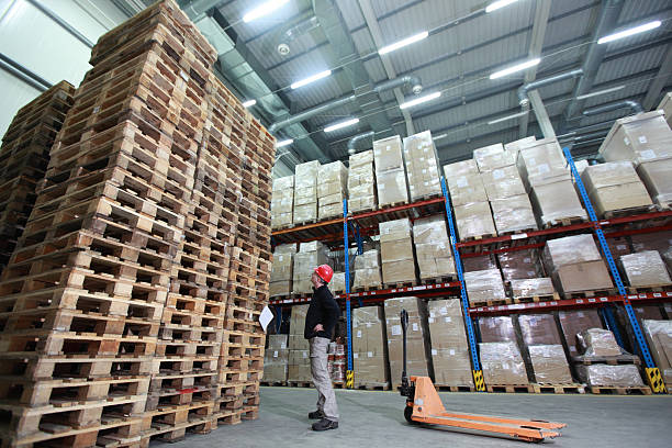 worker,hand pallet truck, stack of wooden pallets in storehouse stock photo