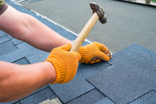 Workers hands installing bitumen roof shingles using hammer in nails. stock photo