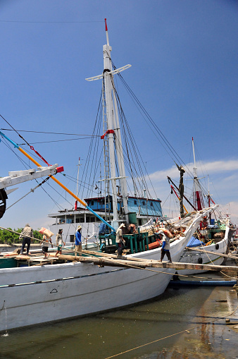 Jakarta, Java, Indonesia: manual work is used to load cargo into a pinisi ship at Sunda Kelapa harbor - bags are carried on the shoulders of works over a fragile gangplank - old port on the Ciliwung River estuary, once the main port of Sunda Kingdom of Pajajaran and a Portuguese outpost.
