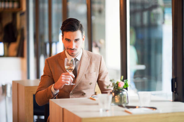 Working even at the restaurant Handsome young Caucasian ethnicity businessman drinking a glass of white wine in a nice upscale restaurant. casanova stock pictures, royalty-free photos & images