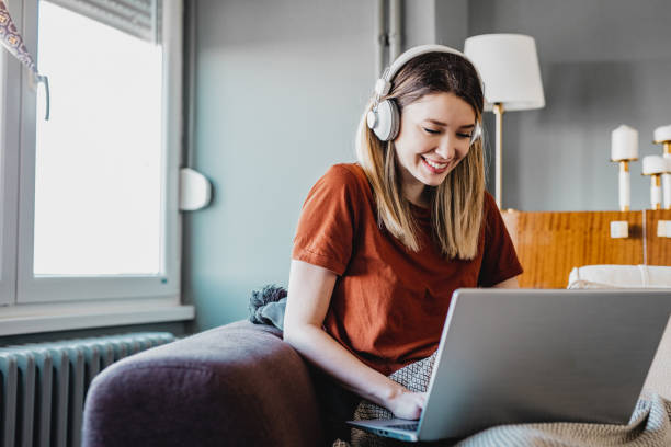 Working from home Young woman is using laptop and working in the living room headphones photos stock pictures, royalty-free photos & images